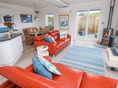 A living room with red sofas blue cushions a wood burning stove and a dining area with wicker chairs at Petroc in Portreath