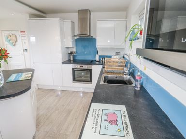 A kitchen with white cabinets black countertops a stainless steel oven a sink and a blue backsplash at Petroc in Portreath