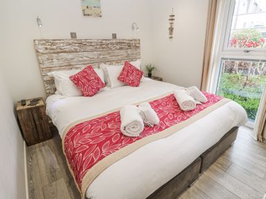 A bedroom with a large bed red patterned cushions and a window at Petroc in Portreath