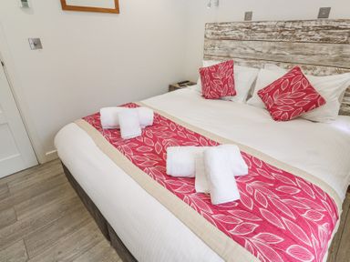 A bedroom with a bed with white linens red leaf patterned runner and pillows with rolled white towels on the bed at Petroc in Portreath