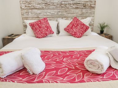 A bed with red leaf patterned cushions and runner with rolled white towels on top at Petroc in Portreath