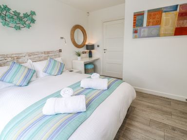 A bedroom with a bed with white linens and striped pillows and blanket a round mirror on the wall and a bedside table with a lamp at Petroc in Portreath
