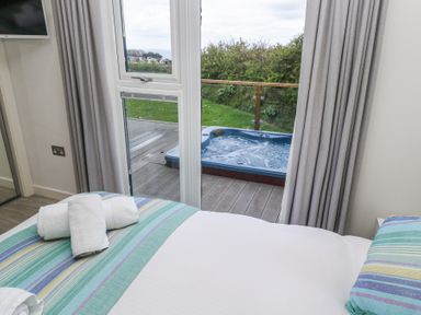 A bedroom with a bed and towels looking out to a balcony with a hot tub and green bushes at Petroc in Portreath