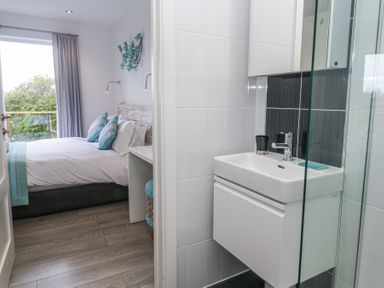A small bathroom with sink and mirror cabinet next to a bedroom with bed and pillows at Petroc in Portreath