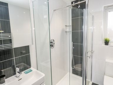 A bathroom with a glass shower enclosure a white sink a toilet and a small plant on a window sill at Petroc in Portreath