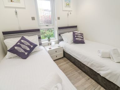 A bedroom with two single beds white bedding purple fish patterned pillows a central nightstand and a window at Petroc in Portreath