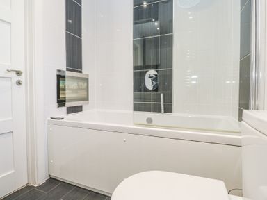 A bathroom with a white bathtub a mounted television and tiled walls at Petroc in Portreath