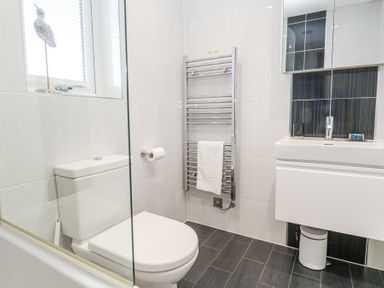 A bathroom with a white toilet, a towel rack with a towel, a sink with a cabinet, and a window at Petroc in Portreath