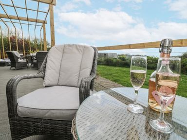 An outdoor seating area with cushioned wicker chairs a glass table with two glasses of sparkling wine and a bottle on a deck at Petroc in Portreath