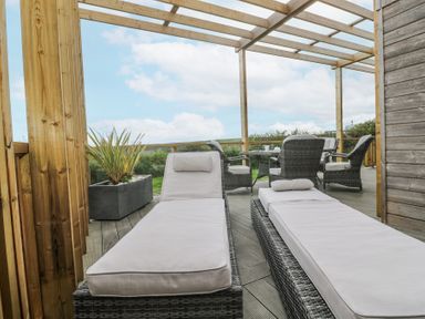 An outdoor deck with two cushioned lounge chairs a table with four chairs and a planter under a wooden pergola at Petroc in Portreath