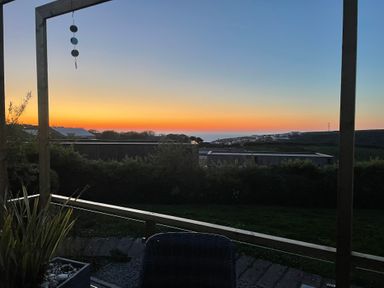 A sunset view over houses and greenery framed by a wooden structure at Petroc in Portreath