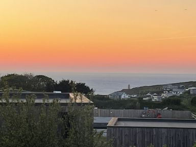 A sunset over the ocean with a coastal village and buildings in the foreground at Petroc in Portreath
