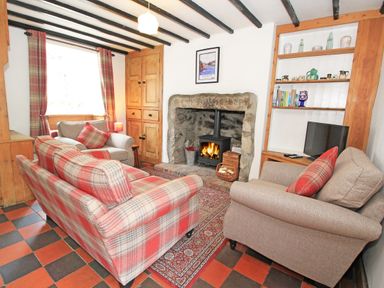 A living room with sofas around a fireplace and a TV on a shelf at Ivy House in Beddgelert