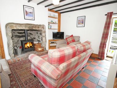 A sitting room with a fireplace a wood stove a plaid sofa and armchair a rug and a television at Ivy House in Beddgelert