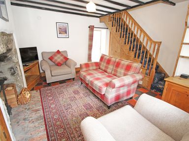 A living room with a plaid sofa armchairs a TV on a wooden stand a patterned rug and wooden stairs at Ivy House in Beddgelert