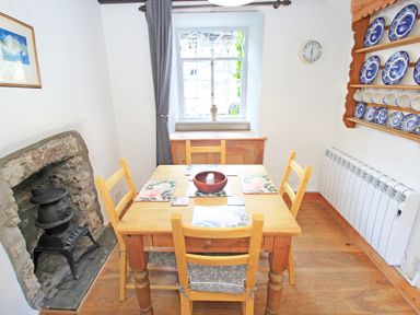 A dining room with a wooden table and chairs a window and a stone fireplace at Ivy House in Beddgelert