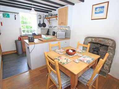 A kitchen with a wooden dining table and chairs next to a stone fireplace at Ivy House in Beddgelert