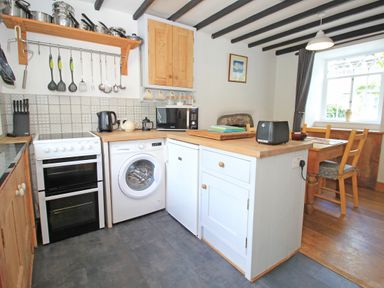 A kitchen with stove microwave washing machine toaster dining table and window at Ivy House in Beddgelert