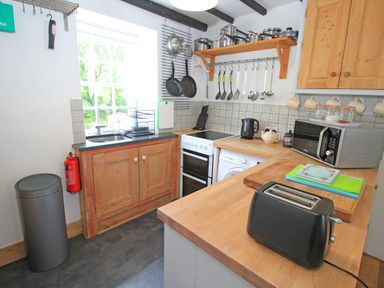 A kitchen with wooden cabinets and counter with toaster microwave and various utensils at Ivy House in Beddgelert