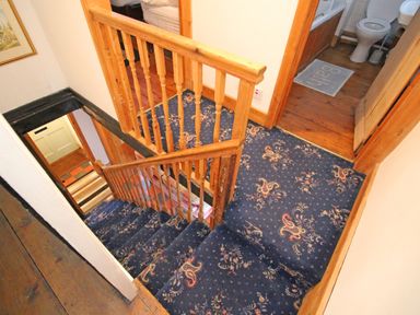 A staircase with blue patterned carpet and wooden handrail leading to a hallway with wooden floor and bathroom at Ivy House in Beddgelert