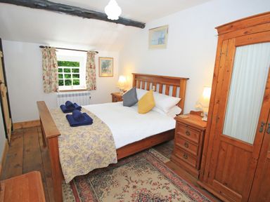 A bedroom with a wooden double bed a wardrobe bedside tables and a window with floral curtains at Ivy House in Beddgelert