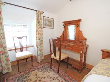 A wooden vanity table with mirror and two chairs near a window with floral curtains in a bedroom at Ivy House in Beddgelert