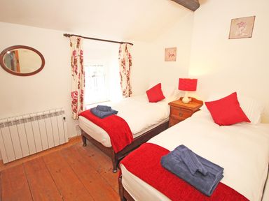 A bedroom with two single beds red cushions and throws bedside table lamp window with floral curtains at Ivy House in Beddgelert
