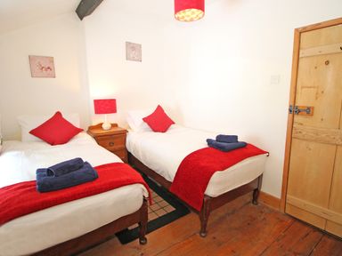 A bedroom with two single beds with red throws and pillows a wooden bedside table with lamp and wooden floor at Ivy House in Beddgelert