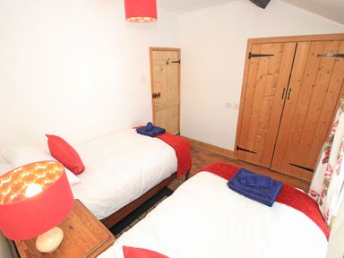 A bedroom with two single beds a wooden wardrobe a wooden door and a side table with a lamp at Ivy House in Beddgelert