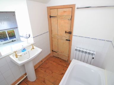 A bathroom with a pedestal sink gold faucets wooden door bathtub and window at Ivy House in Beddgelert