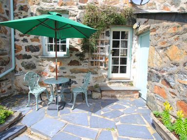 An outdoor patio with a green umbrella over a metal table and chairs next to a stone wall with windows and doors at Ivy House in Beddgelert