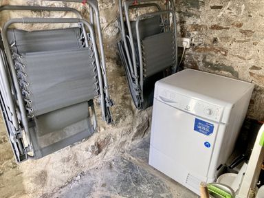 A room with stone walls containing folded chairs hanging on the wall and a white dryer machine plugged into an electrical socket at Ivy House in Beddgelert
