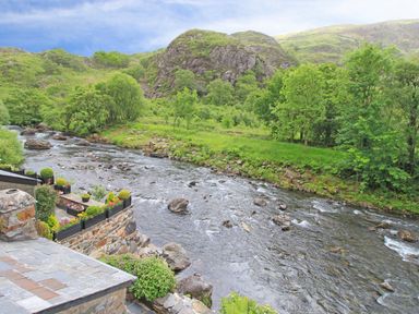 A river flowing through a rocky landscape with green trees and hills in the background at Ivy House in Beddgelert