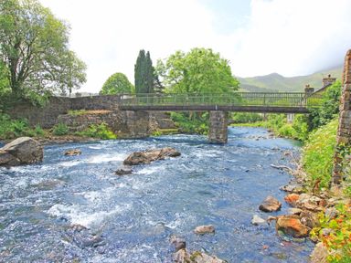 A river flowing under a stone and metal bridge with trees and hills in the background at Ivy House in Beddgelert