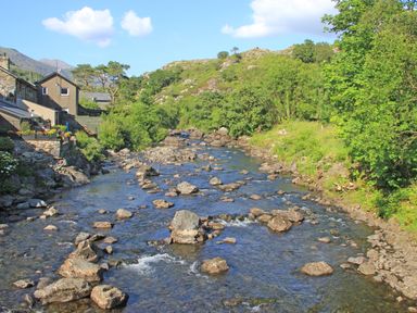 A rocky river flowing between trees and houses at Ivy House in Beddgelert