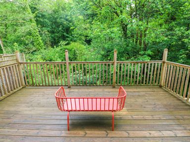 A deck with a red bench surrounded by trees at The Old Creamery in Ffairfach