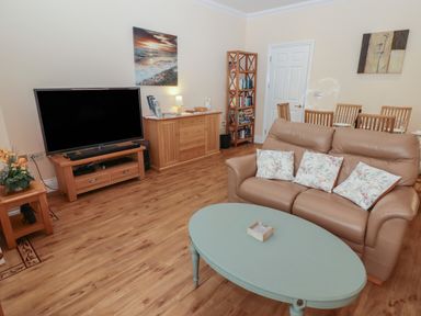 A living room with a brown leather sofa and blue coffee table with a TV and wooden furniture at Apartment 7 Mansion House in Tenby