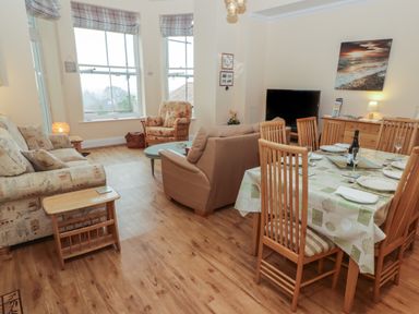 A living room and dining area with wooden flooring a sofa armchair dining table and chairs and a television at Apartment 7 Mansion House in Tenby