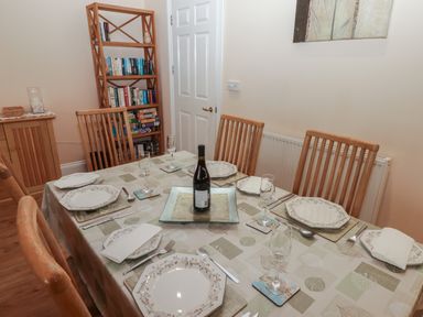 A dining room with a set table including plates glasses and a bottle on the table with a wooden bookshelf in the background at Apartment 7 Mansion House in Tenby