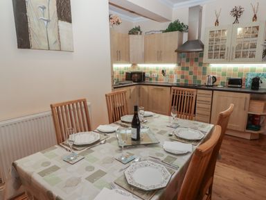 A dining area with a set table and chairs next to a kitchen with wooden cabinets and tiled backsplash at Apartment 7 Mansion House in Tenby