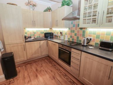 A kitchen with wooden cabinets a stove a microwave a kettle and a toaster at Apartment 7 Mansion House in Tenby