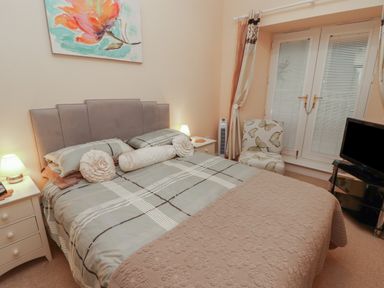 A bedroom with a bed bedside tables a chair and a television at Apartment 7 Mansion House in Tenby