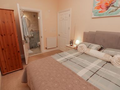 A bedroom with a bed a bedside table with a lamp and a wooden wardrobe near an open door to a bathroom at Apartment 7 Mansion House in Tenby