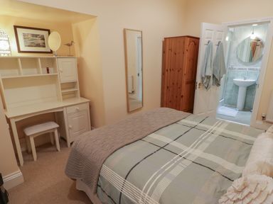 A bedroom with a bed a desk a wardrobe a wall mirror and an open door to a bathroom at Apartment 7 Mansion House Tenby