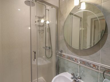 A bathroom with a glass shower enclosure a round mirror and a sink at Apartment 7 Mansion House in Tenby