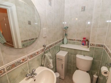 A bathroom with a toilet sink round mirror and small cabinet at Apartment 7 Mansion House in Tenby