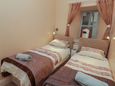 A bedroom with two single beds separated by a small white nightstand under a window with blinds and sheer curtains at Apartment 7 Mansion House in Tenby