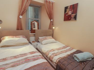 A bedroom with two single beds a small nightstand a window with curtains and a small mirror at Apartment 7 Mansion House in Tenby