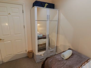 A bedroom with a bed covered in a brown bedspread and a rolled towel on top next to a white wardrobe with mirrored doors and a blue bag on top at Apartment 7 Mansion House in Tenby
