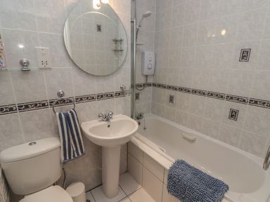 A bathroom with a toilet sink round mirror and bathtub at Apartment 7 Mansion House in Tenby
